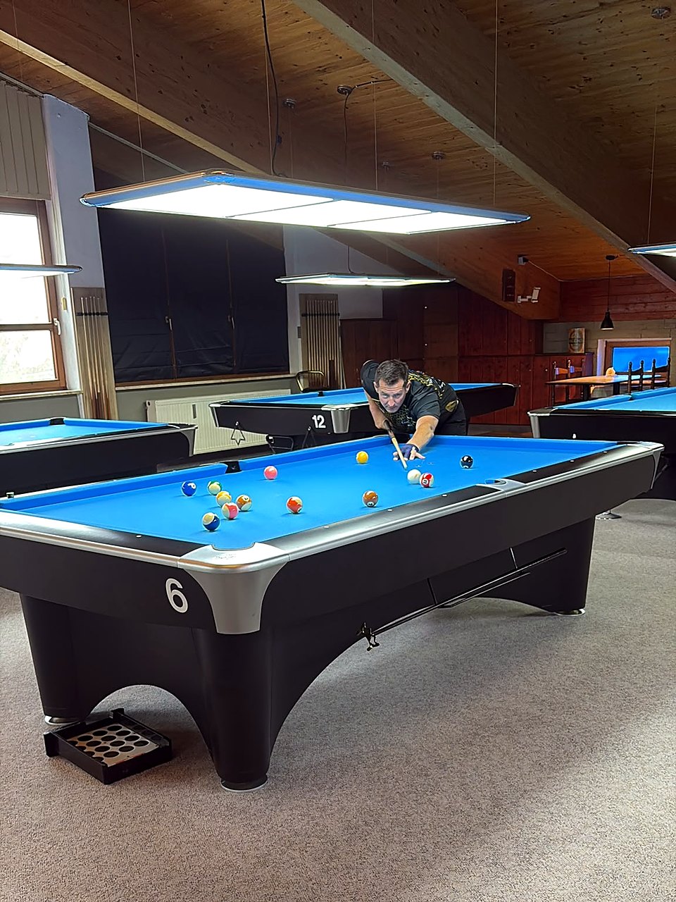 Ein Spieler der 3. Mannschaft des BSV Playhouse FFB beim Stoß an einem blauen Pool-Billardtisch, im Hintergrund weitere Tische