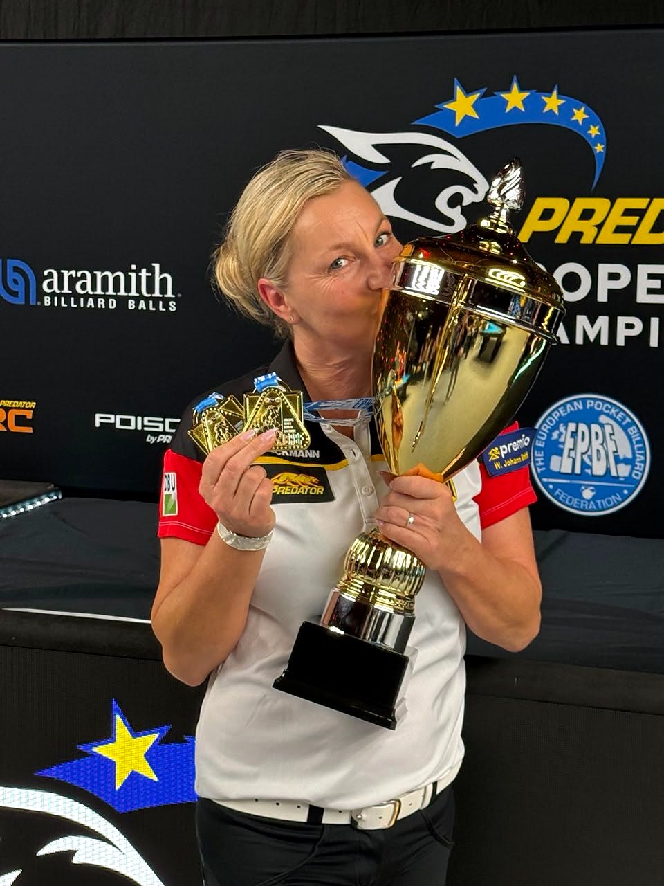 Yvonne Ullmann-Hybler küsst den goldenen Pokal und hält zwei Goldmedaillen in der Hand, im Hintergrund die Wand der Predator European Pool Championships